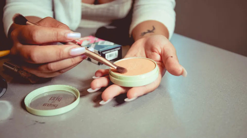 Hände tragen mit einem Pinsel Puder aus einer Kompaktdose auf